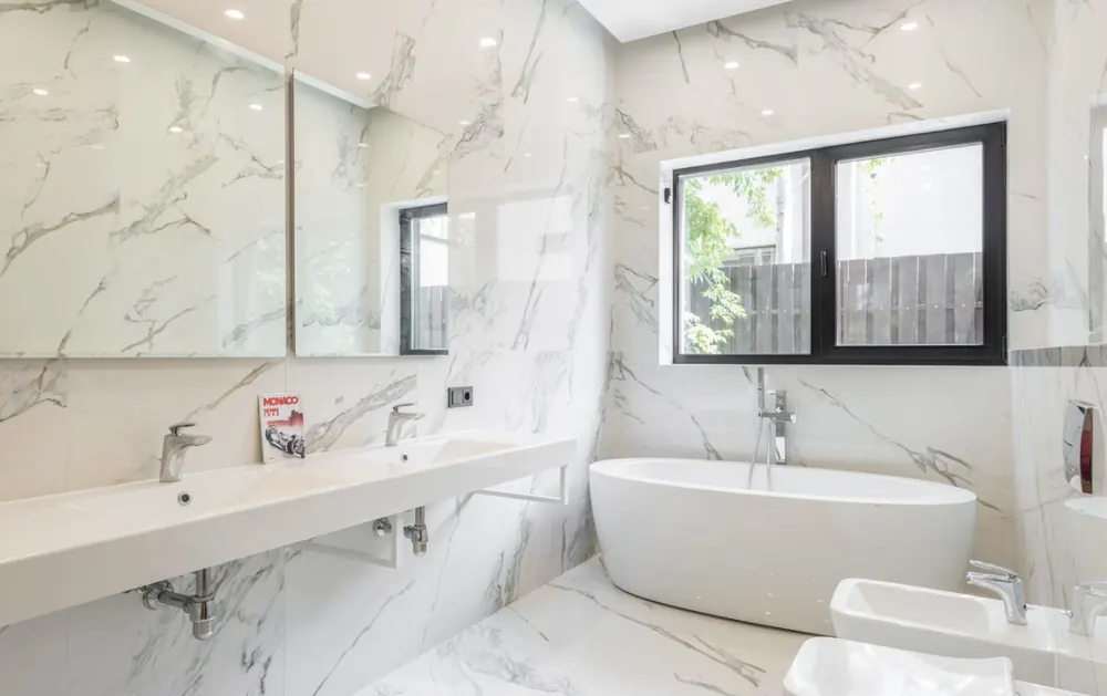 Baño en suite con bañera exenta, doble lavabo suspendido y revestimiento efecto mármol